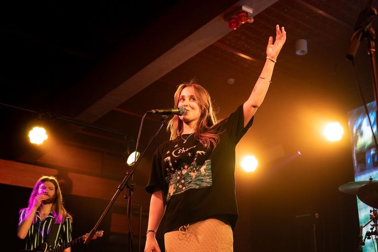 Sammy Gilchrist of The Fuss singing into a microphone with one hand raised on stage, photographed by Mitchell Jarrett.